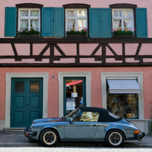 Bilden föreställer en snygg grön porsche som står parkerad invid ett rosa hus med gröna fönsterluckor